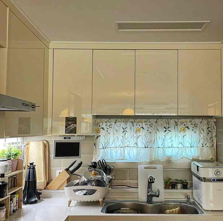 A white and beige toned kitchen featuring floral curtains and organized kitchen tools with a warm atmosphere