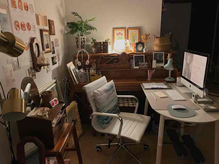 Natural-toned home office space featuring vintage wooden furniture and white desk, highlighted by warm mood lighting and wall decor in the workspace