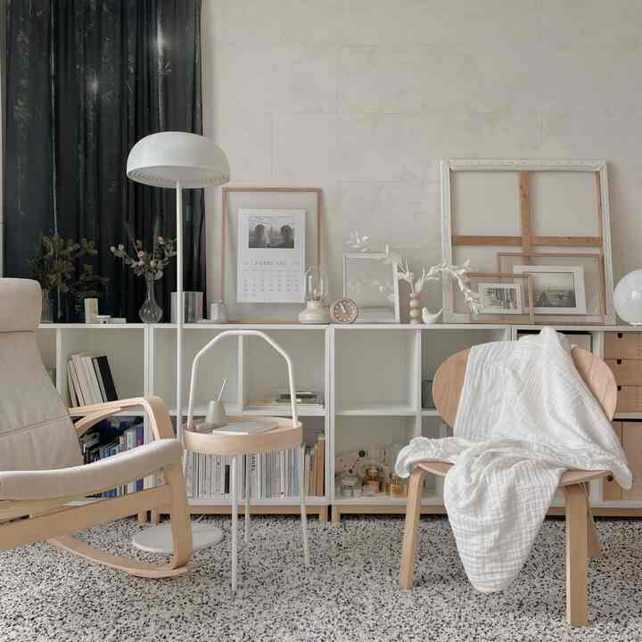 A natural-toned living room featuring white and wood elements, simple chairs, a rug, and various picture frames arranged neatly