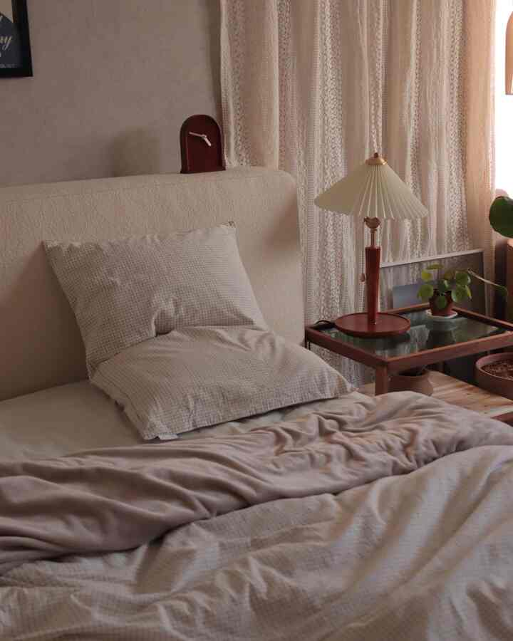Beige and ivory toned bedroom featuring lace curtains and vintage-style table lamp creating a cozy atmosphere