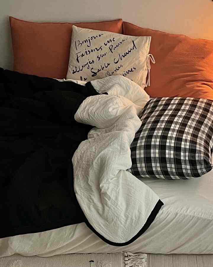 Beige-toned bedroom featuring white and black bedding, cushions, and a quilt creating a cozy atmosphere