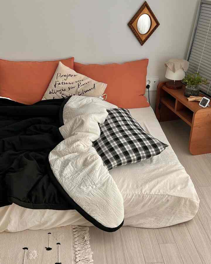 Natural tone bedroom featuring ivory mattress, black blanket, and orange pillows with minimalistic ambiance