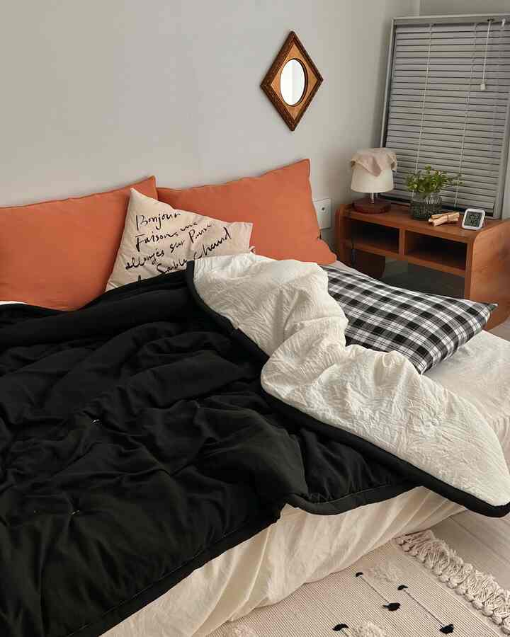 Natural toned bedroom featuring black and white bedding with orange cushions, creating a cozy atmosphere