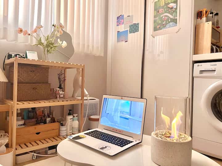 白と木目調が調和した5坪のワンルーム、棚やノートパソコン、ミニ室内暖炉が配置された雰囲気のある空間