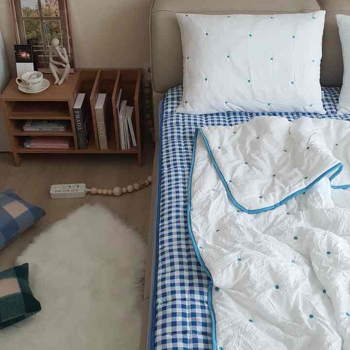 白と青のトーンの寝室、ベッドと寝具、木製の本棚が配置されたナチュラルで落ち着いた雰囲気のインテリア