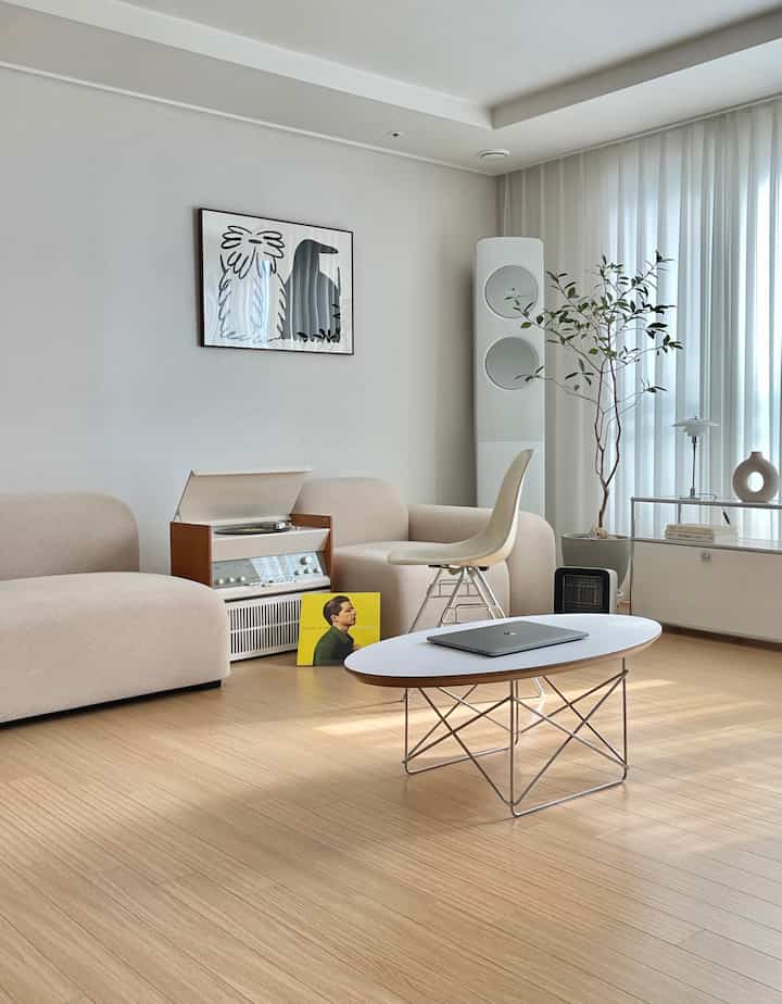 ナチュラルトーンの床とベージュのソファが配置された白いリビング、シンプルなデザインとミッドセンチュリーモダンの雰囲気あるインテリア