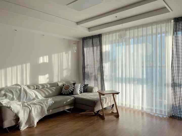 A natural modern living room with white walls, brown wood flooring, gray sectional sofa, and checkered curtains creating a cozy atmosphere