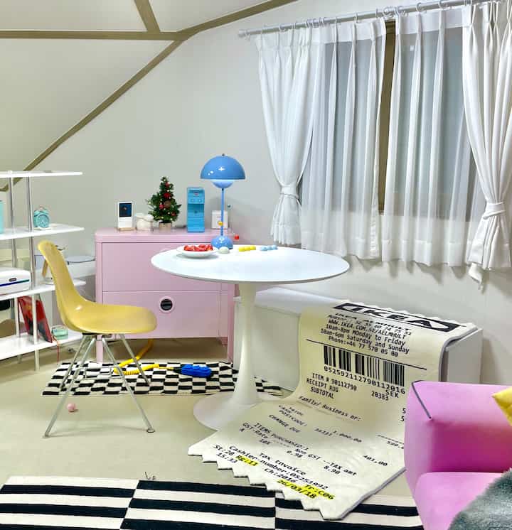 白とピンクのトーンのワンルーム、明るいダイニングテーブルとピンクのチェスト、黄色の椅子が温かみのある雰囲気を作るインテリア