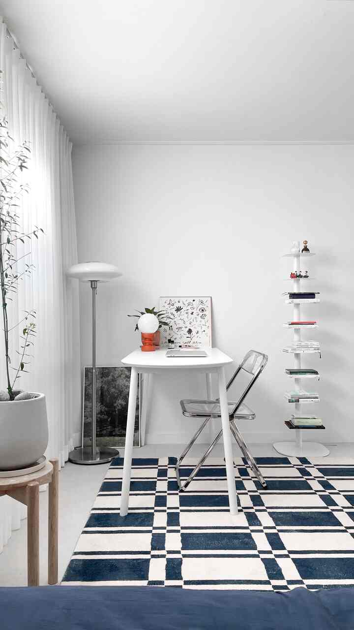 White and navy-toned bedroom featuring a central desk and transparent chair, creating a cozy workspace atmosphere