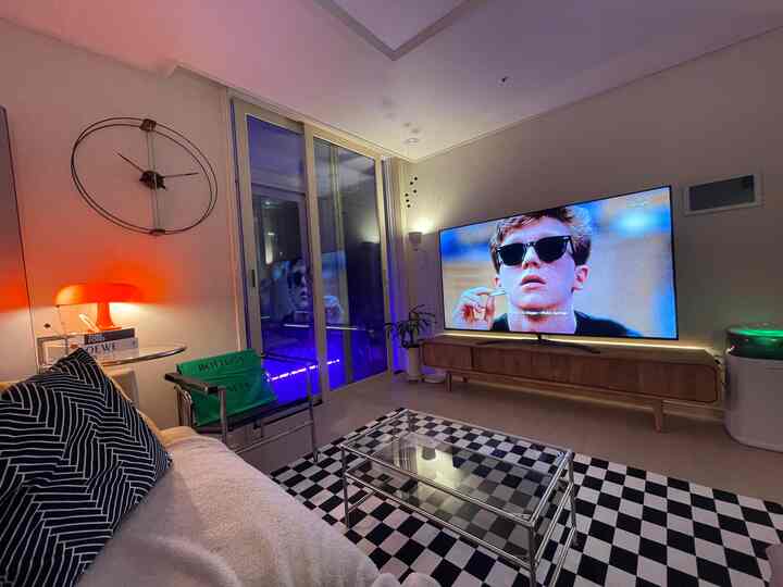 A modern living room dominated by white and black tones in mid-century modern style, featuring a checkerboard rug, glass coffee table, and large TV