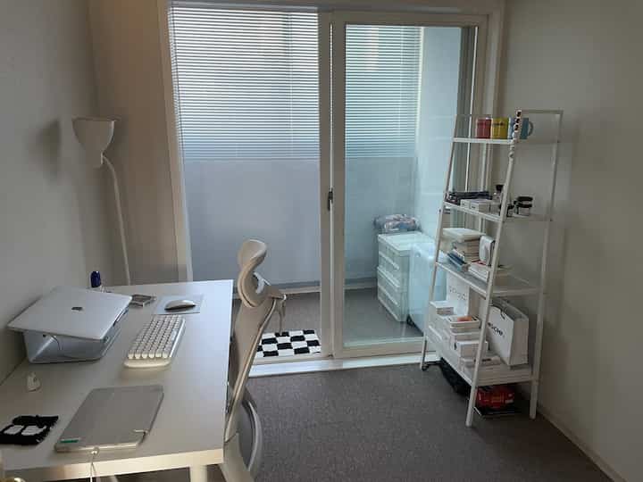 White and black toned small home office featuring a desk, chair, and shelf next to a window, creating a clean workspace