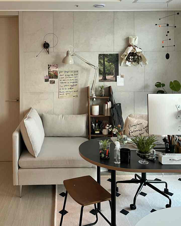 Natural toned living room home office featuring beige sofa, black table, wooden shelf, and plants with cozy atmosphere