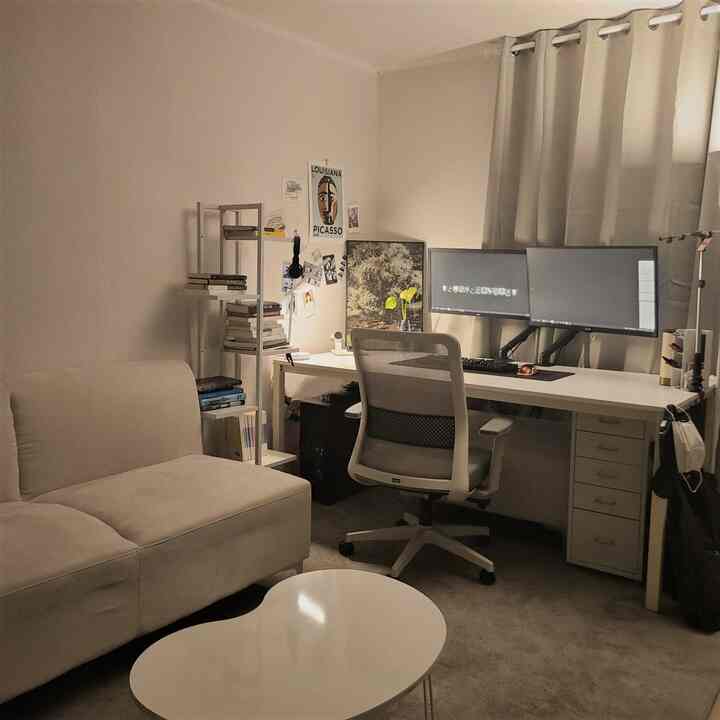 ホワイトとベージュのトーンの小さなワンルーム、ソファとデスクが配置されたシンプルでミニマルなホームオフィス空間