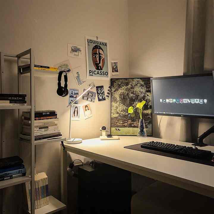 暖かみのあるトーンのワンルームホームオフィス、ホワイトデスクと本棚が配置され、コンピューターモニターとデスクランプが調和した空間