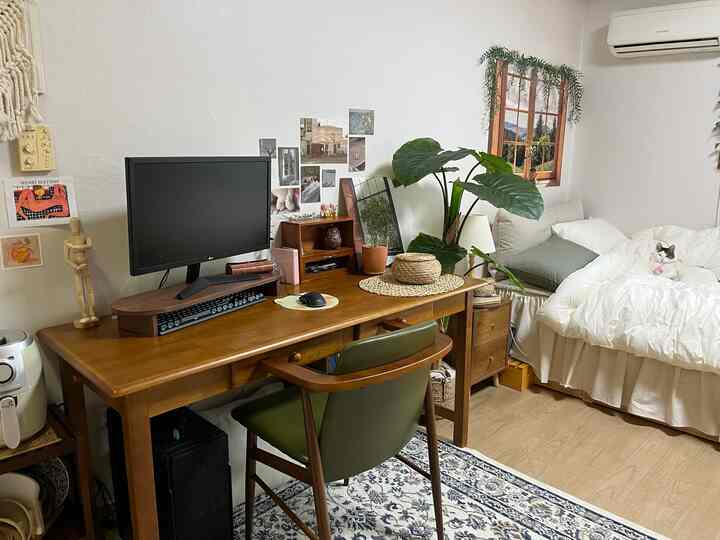 ホワイトの寝具と木目調デスクがあるナチュラルな寝室、猫と植物が配置された居心地の良いホームオフィス空間