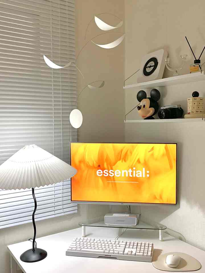 ホワイトトーンのコーナーデスクとアルミブラインド、プリーツランプが配置された清潔感のあるホームオフィスのインテリア