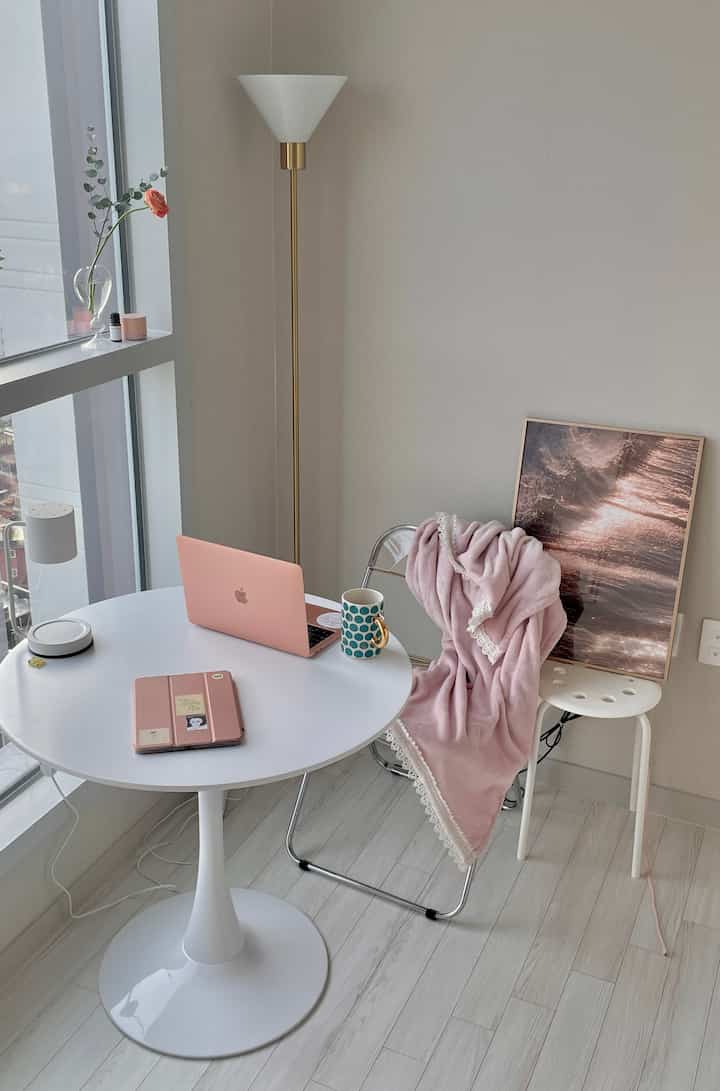 Modern bedroom space featuring white round table, chairs, floor lamp with pink and rose gold tones creating a cozy home office vibe