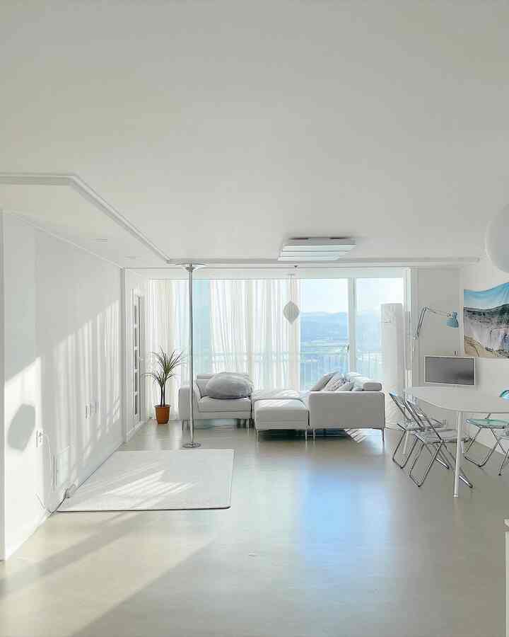 明るい白色調のリビングルーム、白いソファと丸いダイニングテーブル、透明な椅子が配置された清潔で現代的な空間