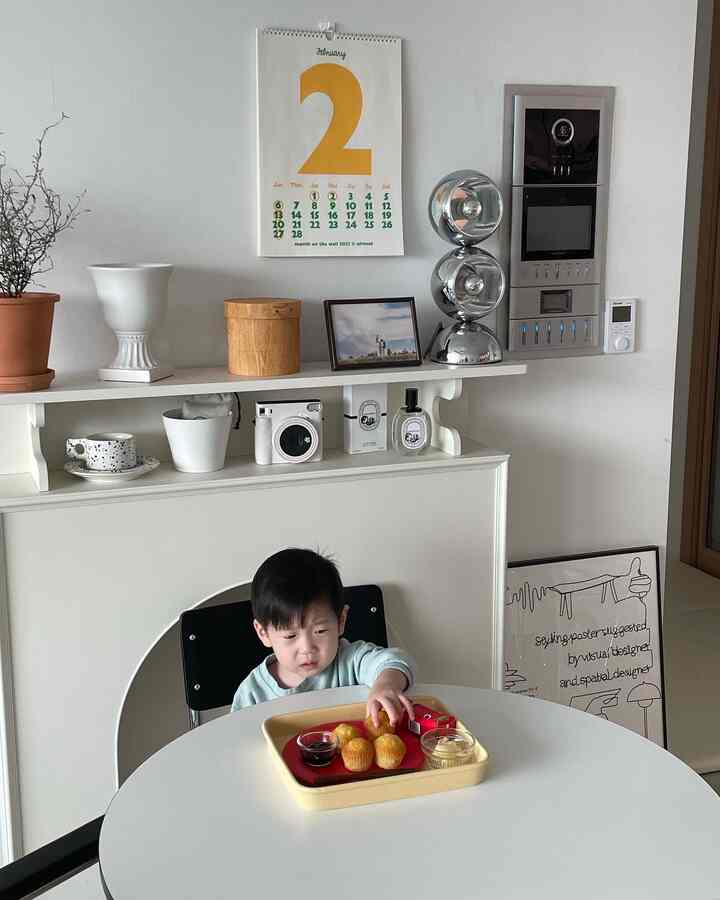 White and natural toned dining room featuring a child eating snacks at a round dining table in a cozy setting