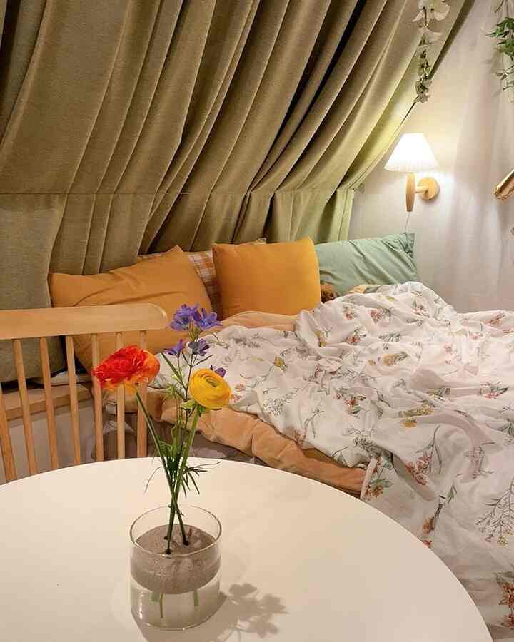 ナチュラルな色調の寝室、花瓶のあるダイニングテーブルと花柄の掛け布団カバー、遮光カーテンが配置された落ち着いた雰囲気のインテリア