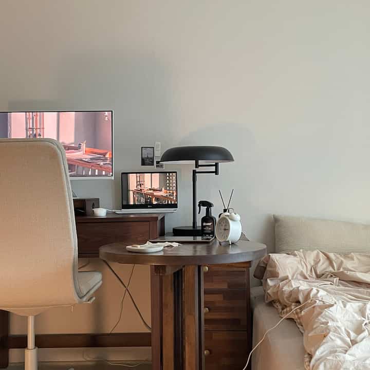 Beige and black toned home office-bedroom featuring wooden table, monitor, and desk lamp creating a cozy atmosphere