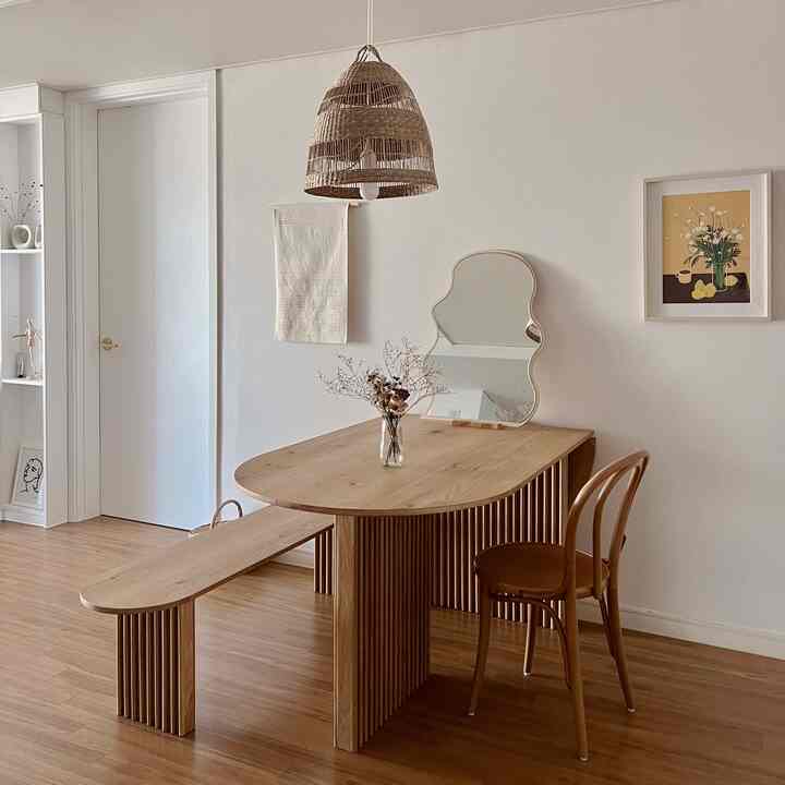 Natural wood-tone living area featuring a wooden dining table, bench, and wave-shaped mirror creating a calm atmosphere