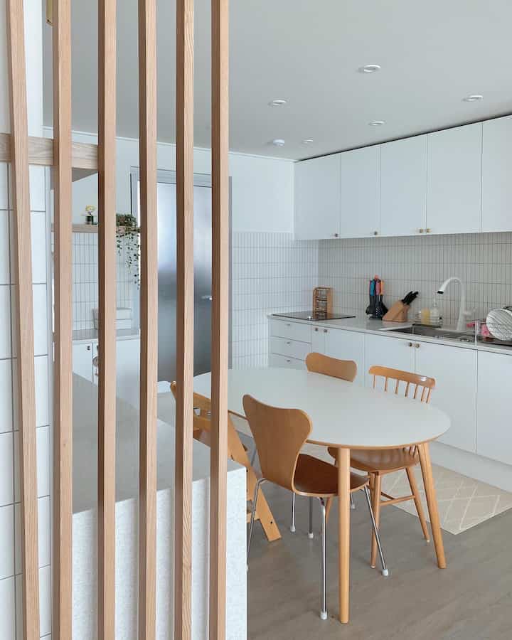 A white and wood tone apartment kitchen featuring a clean, simple dining table and chairs in a neat setting