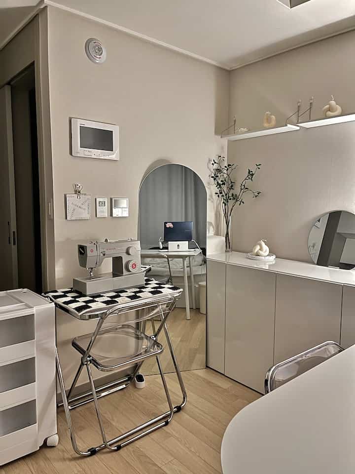 Natural-toned small workspace with white furniture and wood flooring, featuring home office and sewing elements creating a cozy atmosphere