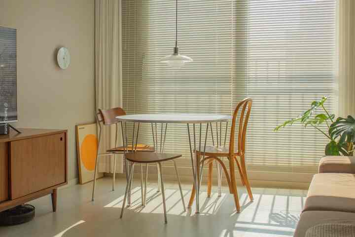 Beige-toned dining room featuring a round white dining table, wooden chairs, and aluminum blinds with natural ambiance
