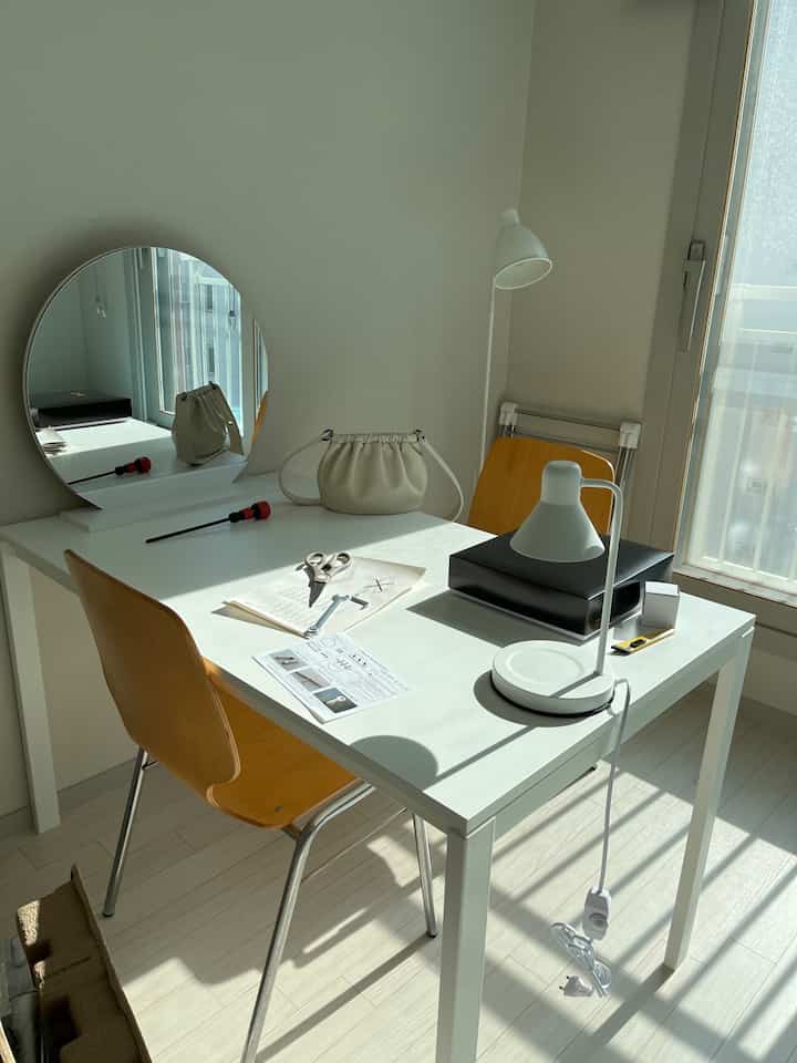Clean white monotone home office with wooden chairs and a round mirror in a simple workspace