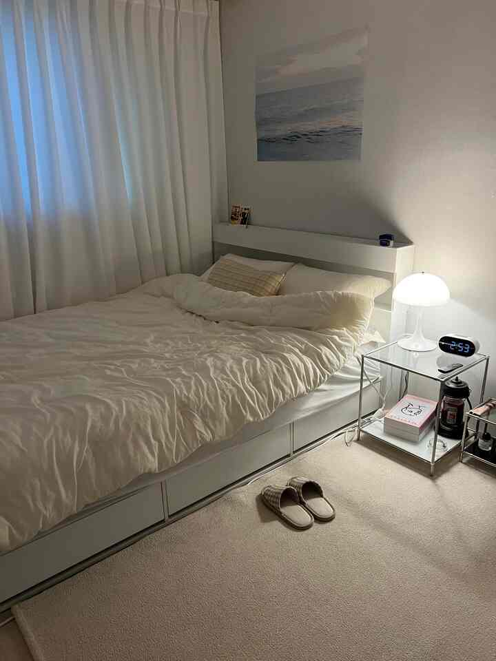 白を基調とした寝室、白いベッドとカーテン、居心地の良い照明が配置されたシンプルなインテリア