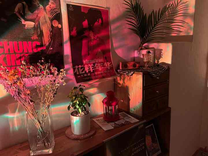 赤と木目調のムード照明が灯る小さなヴィンテージルーム、映画ポスターと植物が配置された印象的な空間