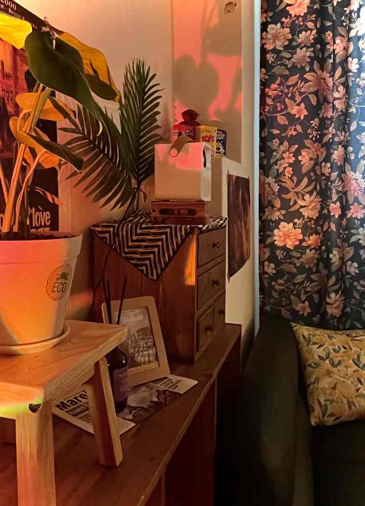 暖かいオレンジ色の光に包まれ、ヴィンテージ家具と緑の植物が配置された小さくコンパクトなリビングルーム