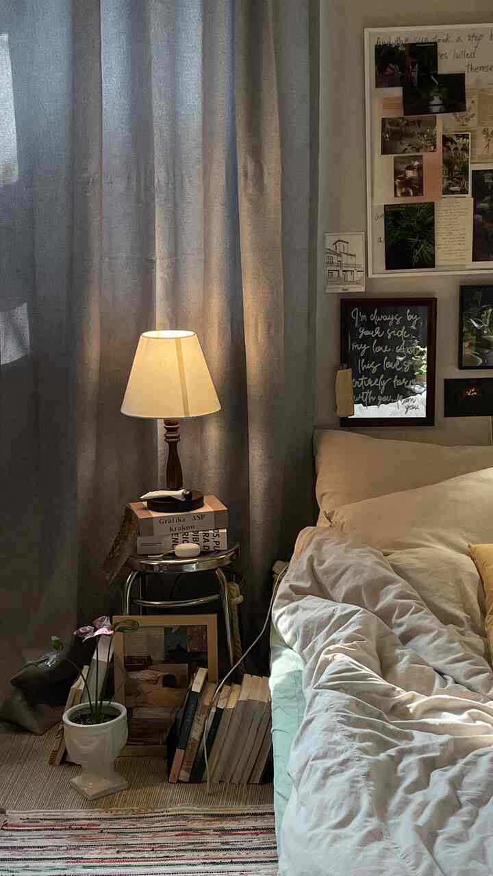 A cozy bedroom in soft beige and gray tones featuring a table lamp, curtains, and books neatly arranged