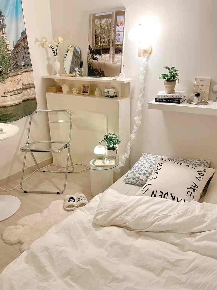 Bright white-toned bedroom featuring a bed, shelf, and simple cozy decor