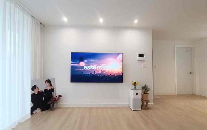 A clean and simple modern living room with dominant white and wood tones featuring a wall-mounted TV, air purifier, and white curtains in a bright space