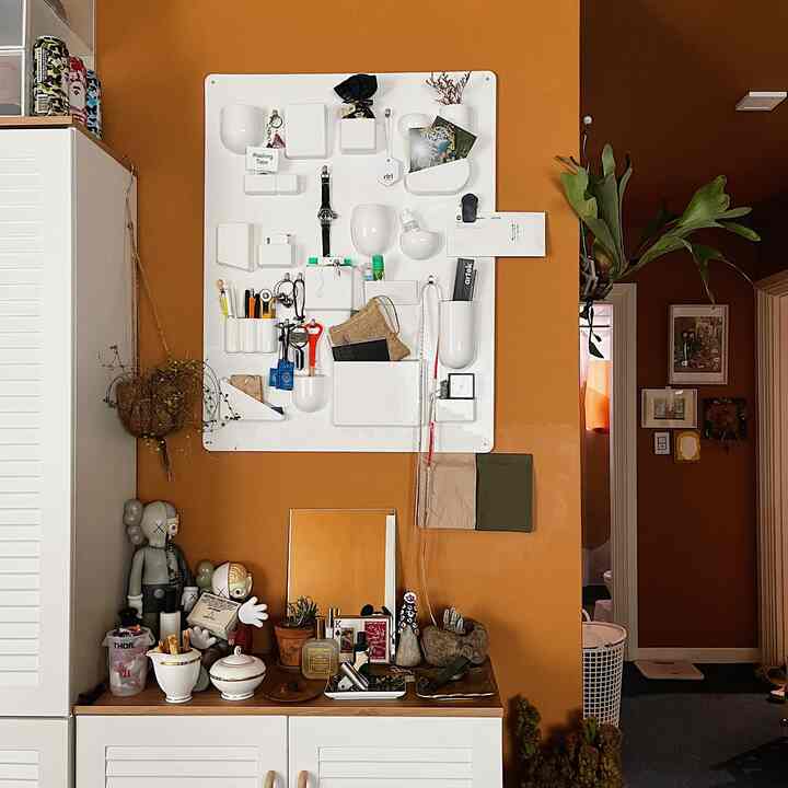 Entrance space with warm orange walls and white wall-mounted organizer, featuring natural decorative objets and plants for a cozy vibe