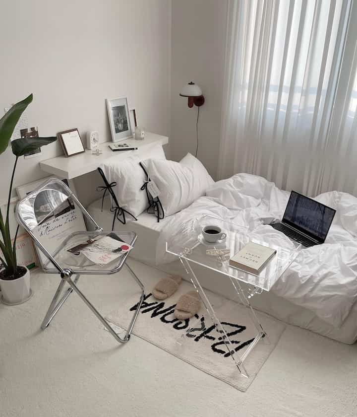 Bright white bedroom featuring a transparent chair and acrylic table, creating a clean and airy atmosphere