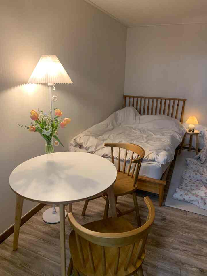 Wood tone and white bedroom featuring round dining table with chairs, bed, and floor lamp creating a cozy atmosphere