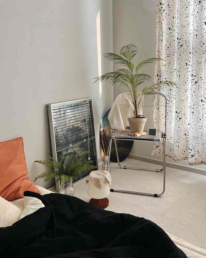 ナチュラルな色調の寝室、柔らかなアイボリーのラグと透明な折りたたみ椅子、植物が配置された落ち着いた空間