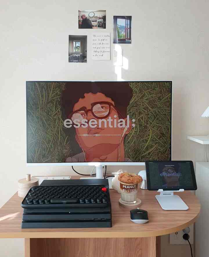 Clean home office space with a white wall, wood tone desk featuring monitor, keyboard, and tablet