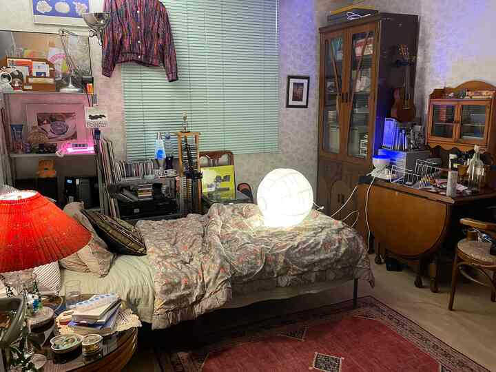 Vintage bedroom featuring red rug, central bed with lighting, and green blinds creating cozy atmosphere