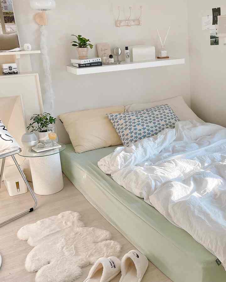 Bright white and soft green bedroom featuring mattress, pillows, and wall shelf with a cozy and natural atmosphere