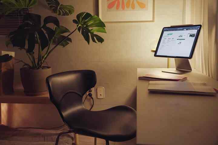 White and green toned home office space featuring black chair, tablet on desk, and Monstera plant creating a cozy work environment
