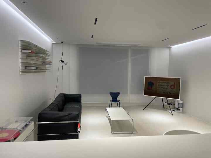 A modern living room in white and black tones, featuring a black leather sofa, white coffee table, and tripod TV stand in a simple layout