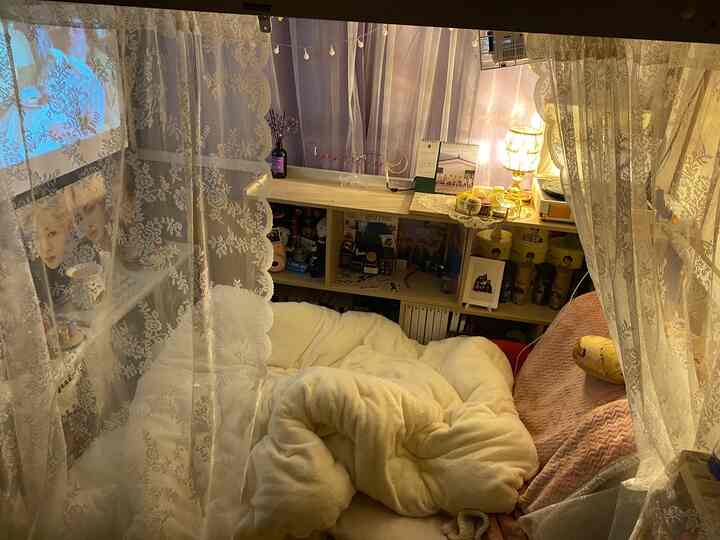 Ivory and pink toned bedroom featuring cozy bedding, lace curtains, and a decorative shelf display in a warm, inviting space