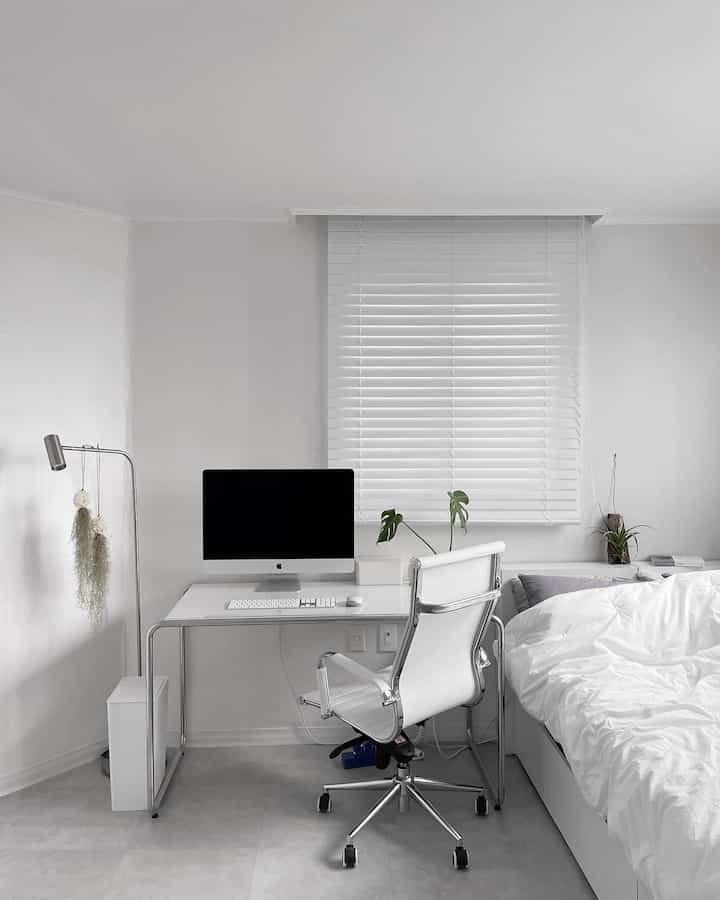 White-toned bedroom and home office space featuring a white desk, office chair, and bed with clean, simple modern design