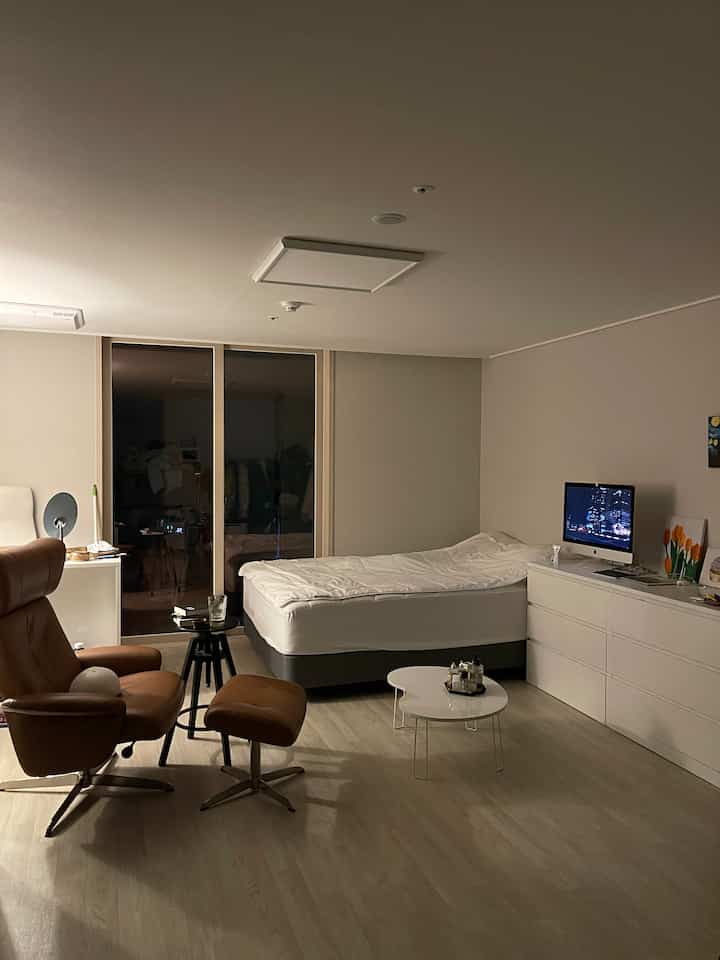 White and brown toned studio bedroom featuring a recliner, bed, and coffee table in a cozy setting