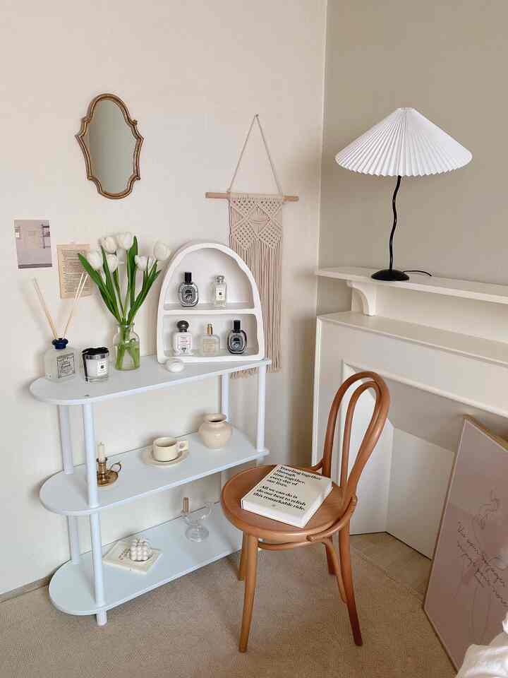 ナチュラルカラーと白を基調としたパウダールーム、3段の白い棚に化粧品と花瓶、曲線的な木製椅子が配置された落ち着いた空間
