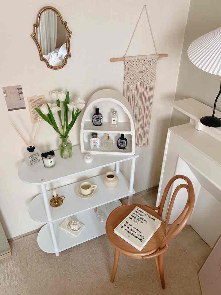 ベージュの壁と木目調チェアがあるナチュラルカラーのミニリビング、白い3段棚とマクラメの壁飾りが暖かい雰囲気を演出するインテリア